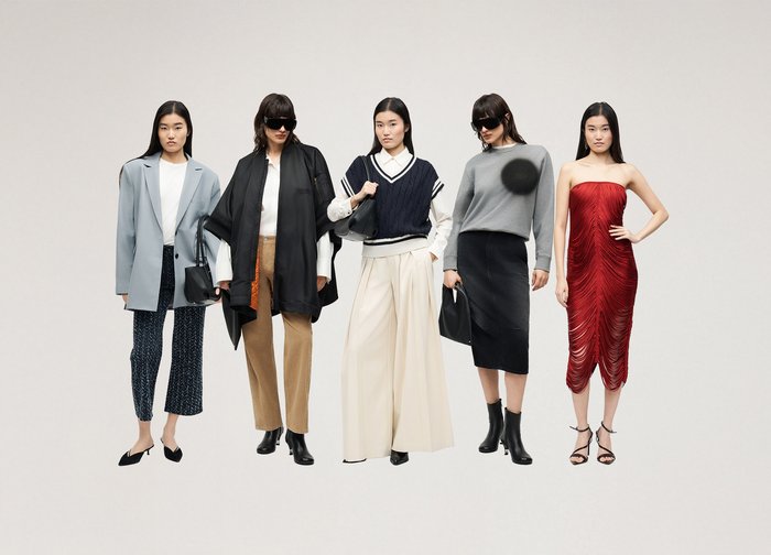 Πέντε γυναίκες στέκονται με διαφορετικές μοντέρνες ενδυμασίες: γκρι σακάκι, φαρδύ μαύρο παλτό, ναυτικό γιλέκο, γκρι πουλόβερ και κόκκινο φόρεμα χωρίς τιράντες.