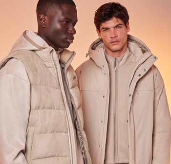 Due modelli indossano un abbigliamento esterno beige chiaro: un gilet imbottito con cappuccio a sinistra e un cappotto con zip e collo alto a destra.