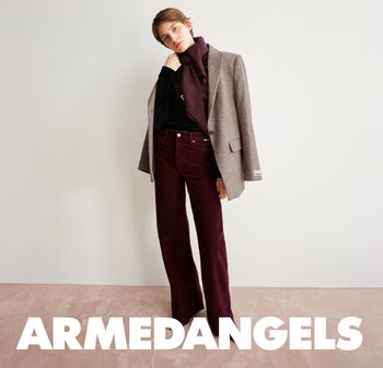 Grau strukturierte Blazer über einem schwarzen Oberteil, kombiniert mit burgunderfarbenen Cord-Trompetenhosen. Der Schal passt zu den Hosen und sorgt für einen harmonischen Look.