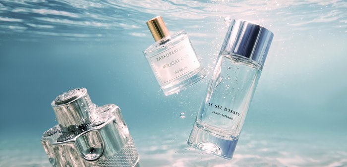 Trois flacons de parfum transparents avec des bouchons argentés et dorés, immergés dans de l'eau claire avec des bulles.