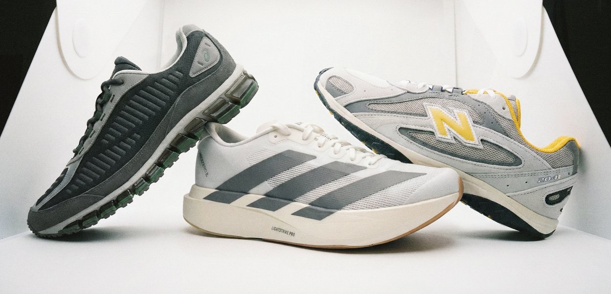 Τρία ζευγάρια αθλητικά παπούτσια: σκούρο γκρι με πράσινες λεπτομέρειες, λευκά με γκρι ρίγες και γκρι με κίτρινο λογότυπο. Ποικιλία υφών και υλικών.