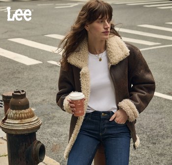 Veste en cuir synthétique marron avec un col et des poignets en fausse fourrure crème, associée à une chemise blanche et un jean bleu, tenant une tasse de café.