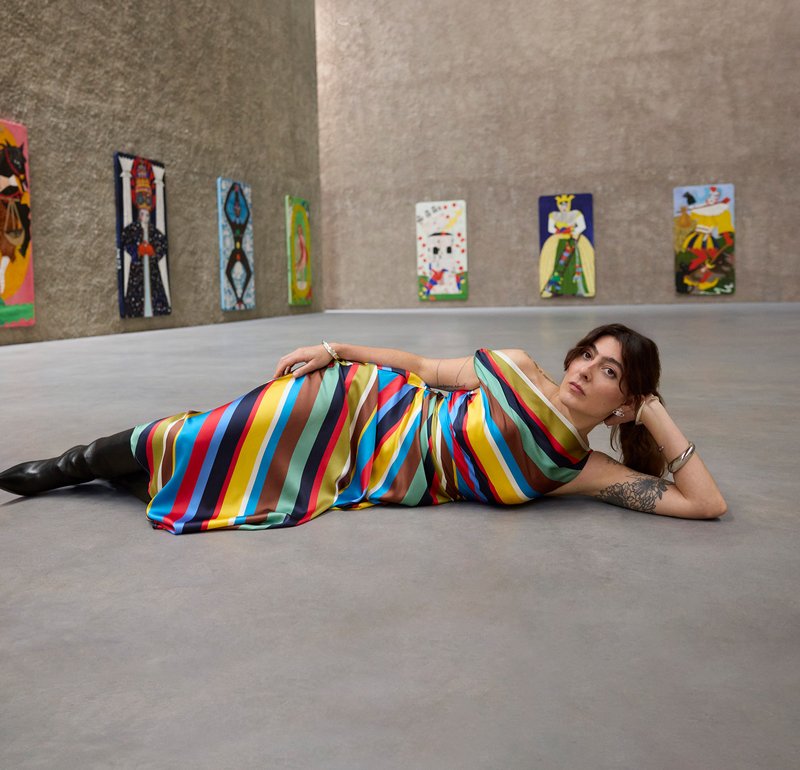 Vestido às riscas coloridas em tecido de cetim, com riscas verticais em vermelho, azul, verde e castanho, combinado com botas pretas até ao joelho.