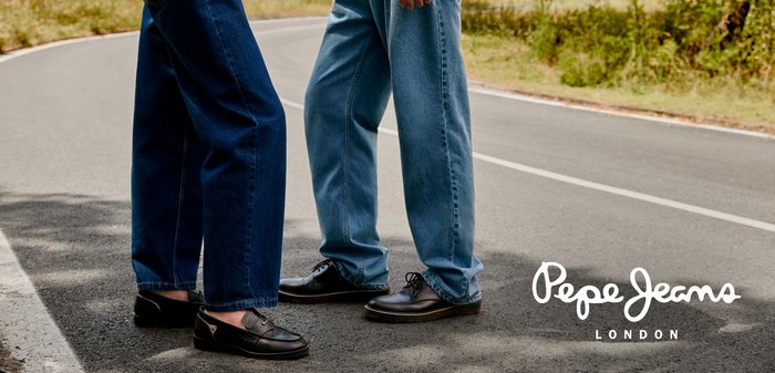Scarpe nere con superficie testurizzata, abbinate a pantaloni blu e denim scuro su una strada. Marchio "Pepe Jeans London" nell'angolo.
