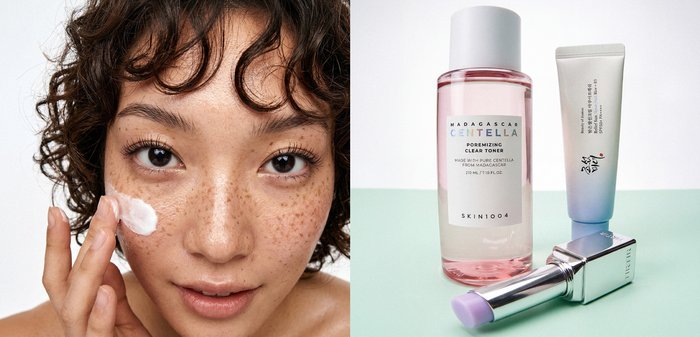 Femme avec des taches de rousseur appliquant une crème blanche sur sa joue, à côté d’une bouteille de tonique, d’un tube de crème et d’un rouge à lèvres teinté de lavande sur une surface claire.