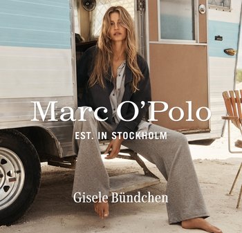 Kobieta o długich włosach, ubrana w luźne szare spodnie i ciemną kurtkę, siedzi boso na stopniu przyczepy kempingowej na piaszczystym terenie na zewnątrz.