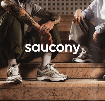 Baskets Saucony en blanc et gris avec une tige en mesh texturé, semelle en caoutchouc contrastante et design à lacets, portées sur des marches en marbre.