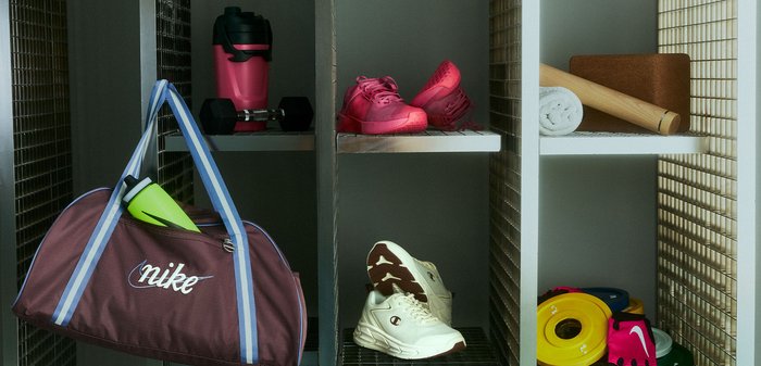 Fitnes omarica z bordo torbo Nike, rdečimi in belimi športnimi copati, plastenkami vode, zvito brisačo, penastim valjčkom in raznimi fitnes dodatki.