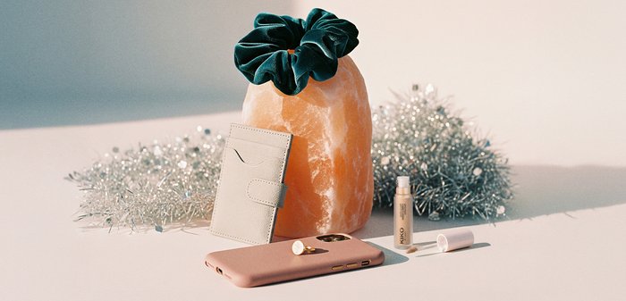 Różowe etui na telefon, jasnoszara kieszeń na karty, złoty sztyft do makijażu, biały tubka pomadki, ciemnozielona gumka do włosów oraz duża pomarańczowa lampa solna.