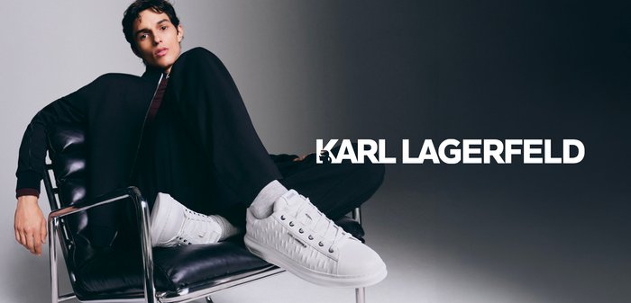 Young person reclining on a black leather chair wearing black clothing and white Karl Lagerfeld sneakers with logo text across the center.