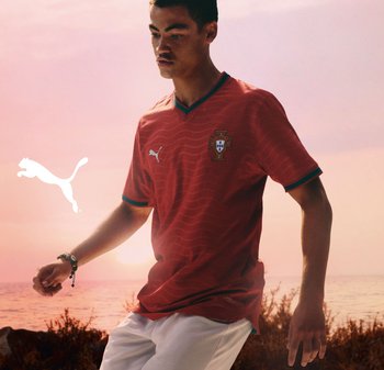 Punainen jalkapallopaita v-kaula-aukkolla, vihreällä reunuksella ja aaltokuvioinnilla. Paidassa on Portugalin kansallisembleemi ja valkoinen Puman logo.