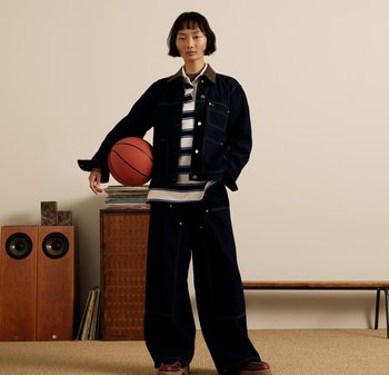 Ciemna dżinsowa kurtka z kieszeniami, zestawiona z pasiastą koszulą i szerokimi spodniami z ciemnego dżinsu. Trzymający piłkę koszykową, stojący na neutralnym tle.