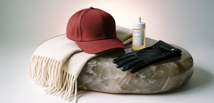 Casquette rouge, écharpe blanche à franges, gants en cuir noir et flacon compte-gouttes de sérum pour le visage disposés sur une surface ronde en marbre.