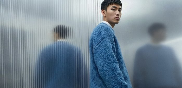 Modrý pletený sveter s textúrovaným povrchom, s okrúhlym výstrihom a spustenými ramenami. Mäkký vzhľad na rozmazanom pozadí.