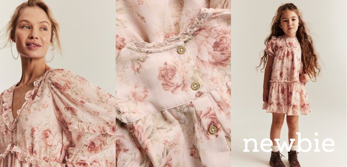 Woman and girl wearing matching pink floral dresses with ruffles, detailed buttons, and puffed sleeves, standing against a neutral background.