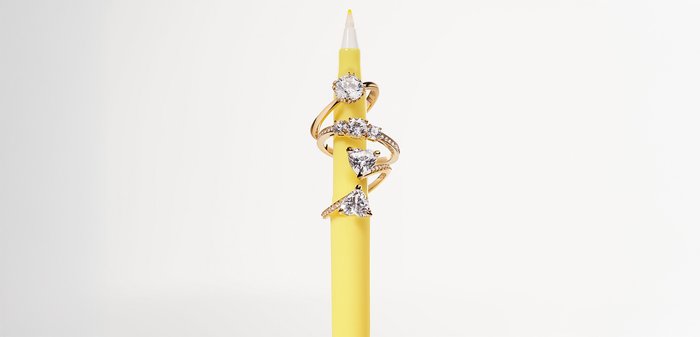 Goldringe mit verschiedenen Diamantformen, darunter rund und birnenförmig, auf einem gelben Bleistift platziert. Auffälliger Schimmer und mehrere Banddesigns.