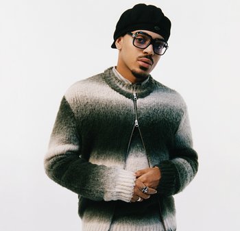 Grau-cremefarbener Gradient-Strickpullover mit hohem Kragen und Reißverschluss, kombiniert mit einem schwarzen Hut und übergroßen Brillen.