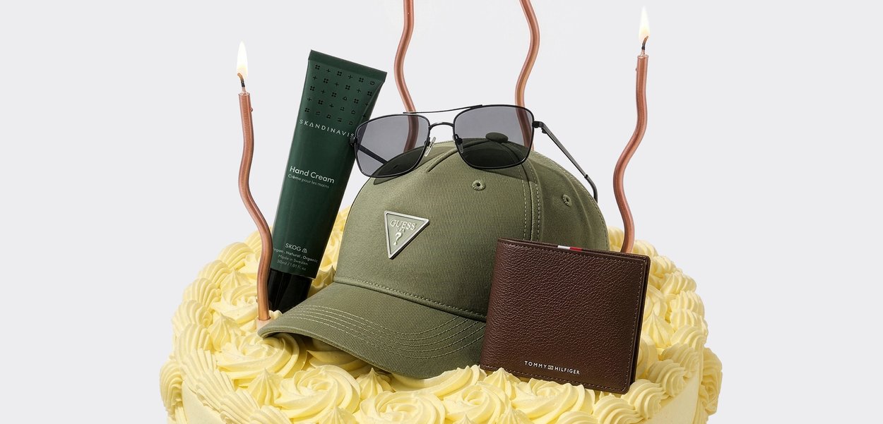 Gâteau jaune glacé surmonté d'une casquette de baseball verte, de lunettes de soleil noires, d'un portefeuille marron et d'un tube de crème pour les mains verte avec deux bougies torsadées allumées.