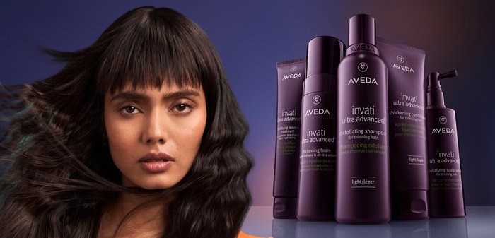 Donna con lunghi capelli scuri fluenti accanto a cinque bottiglie viola di prodotti per la cura dei capelli Aveda Invati Ultra Advanced su una superficie riflettente.
