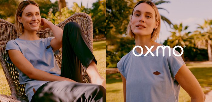 Frau in Schutzkleidung, die entspannt in einem Korbsessel im Freien auf dem Gras sitzt, lächelnd mit einer Hand hinter dem Kopf.