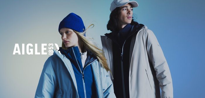 Deux individus portent des vestes de couleurs contrastées : une bleu clair et une beige. La veste bleue a un col montant et une fermeture éclair, tandis que celle beige a une capuche. Un bonnet bleu orne l'une des personnes, complétant sa veste.