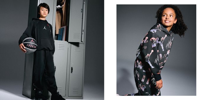 Ung pojke i svart Jordan-träningsdräkt håller en basketboll vid skåpen, bredvid en flicka som ler i en svart Jordan-huvtröja med färgglada tryck.