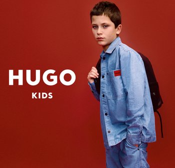 Chemise en denim bleu et pantalon, avec un patch "HUGO", accompagnés d'un sac à dos noir. Fond rouge.