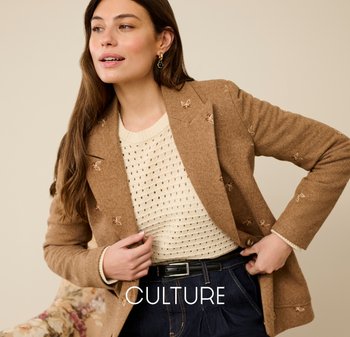 Brauner Blazer mit Struktur und Blumenstickerei, getragen über einem cremefarbenen Strickpullover. Schwarzer Gürtel und dunkle Denim-Hose vervollständigen das Outfit.