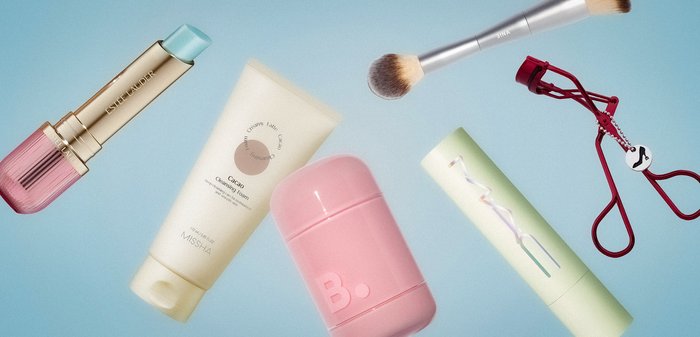 Leppepomade, renseskumtube, rosa beholder, sminkekost, lysegrønn mascara og rød vippekrøller på blå bakgrunn.