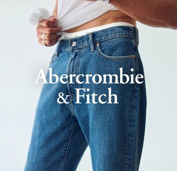 Jeans dżinsowe w średnim niebieskim kolorze o luźnym kroju, z miedzianymi szwami, zapięciem na guziki i markowym paskiem, uzupełnione białą bluzką.