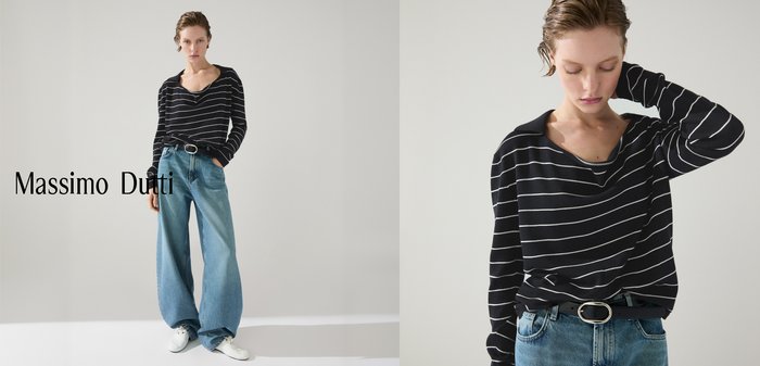 Femme portant un haut à manches longues rayé noir et blanc, un jean bleu et une ceinture noire, regardant vers le bas avec un bras levé derrière son cou.