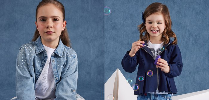 Niña joven con el cabello largo y castaño, vestida con una chaqueta vaquera azul con brillantes y una camiseta blanca, posando frente a un fondo azul.