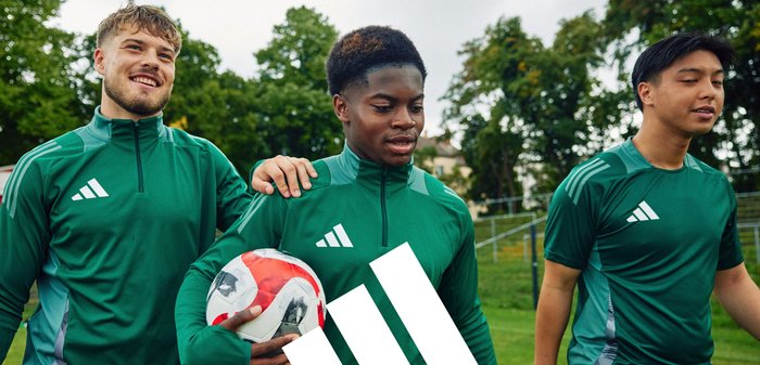 Tre individui in tute sportive verdi con zip e loghi Adidas bianchi stanno insieme, uno di loro tiene un pallone da calcio rosso e bianco.