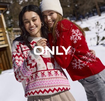 Twee vrouwen staan dicht bij elkaar in de sneeuw. De ene draagt een witte en rode gebreide trui met patroon, de andere een rode trui met witte sneeuwvlokken.