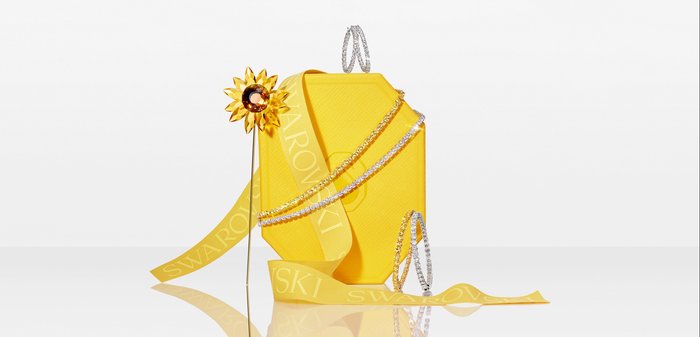 Yellow hexagonal jewelry box with Swarovski ribbon, crystal-studded hoop earrings, two tennis bracelets, and a sunflower-shaped brooch.