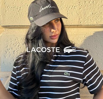 Camisa de polo a rayas blancas y negras con el logo de Lacoste en el pecho, combinada con una gorra negra que presenta el texto "Lacoste" en blanco.