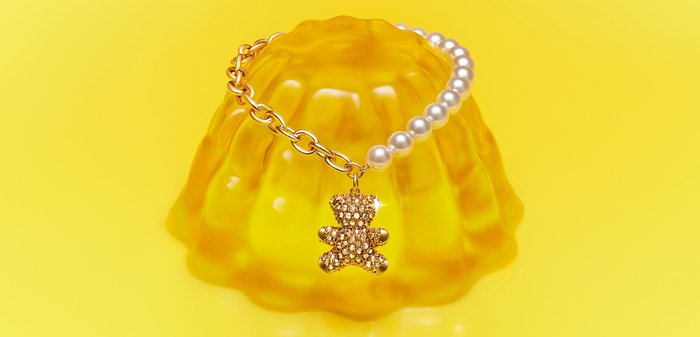 Bracelet en or et perles avec un pendentif ourson étincelant présenté sur un moule à gelée jaune sur un fond jaune vif.