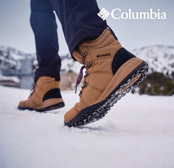 Person, die beige Columbia-Winterstiefel trägt, läuft im Schnee mit verschwommenen Bergen im Hintergrund.