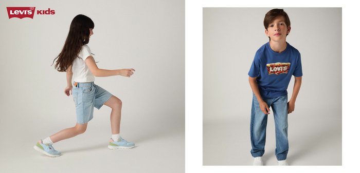 Mädchen in weißem Hemd und Shorts geht, Junge in blauem Levi's-Hemd und Jeans beugt sich vor gegen einen einfarbigen Hintergrund.