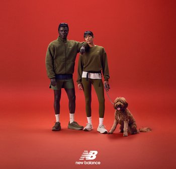 Dos personas con ropa deportiva verde están de pie contra un fondo rojo. Un perro marrón se sienta junto a ellas. Las prendas incluyen camisetas texturizadas y pantalones ajustados.