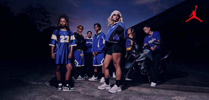 Groupe de sept jeunes adultes en tenue de sport bleue et noire, debout et posant avec assurance en plein air au crépuscule près d'une moto.