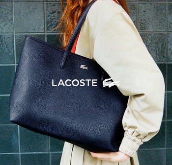 Bolso tote de cuero negro con relieve, con asas largas y un logo metálico de Lacoste. El bolso tiene una forma rectangular espaciosa y una superficie texturizada.