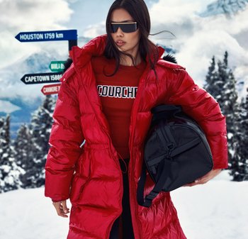 Rød dunjakke med blank finish, med innsnevret midje, brukt over en rød genser med logo. Svart rund veske med skulderrem. Snødekt bakgrunn.