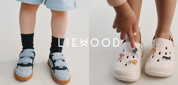 Main d'enfant pointant vers un pendentif tortue sur des sabots beige décorés de pendentifs d'animaux marins, dont une pieuvre, un phoque et une baleine, sur fond blanc.