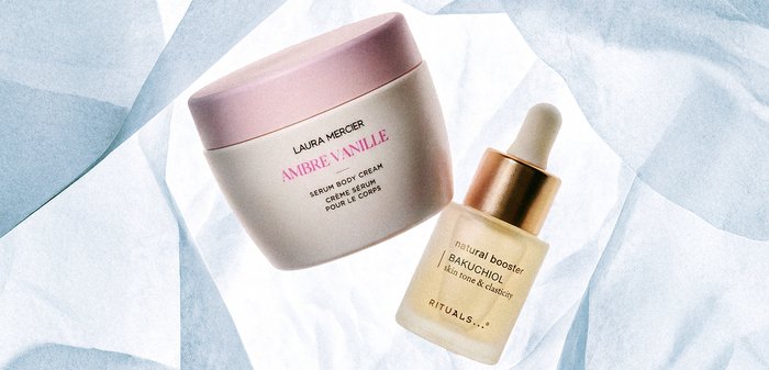 Crème sérum pour le corps Ambre Vanille de Laura Mercier avec un couvercle rose et flacon compte-gouttes Rituals Bakuchiol natural booster, posés sur un papier blanc froissé.