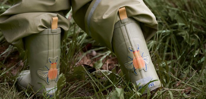 Grüne Gummiregenstiefel mit einem Bienenmuster in Orange und Blau. Verstellbare gelbe Schlaufe, strukturierter Grip und reflektierende Akzente an den Seiten.