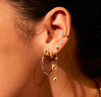 Gouden oorbellen met verschillende ontwerpen: een dikke creool met kleurrijke accenten, een slanke creool, en een ketting met kleine gouden bolletjes en heldere stenen.