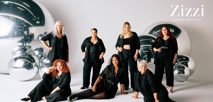 En grupp av sju individer klädda i svarta kläder, inklusive kavajer och byxor, mot en ljus bakgrund med stora metalliska sfärer.