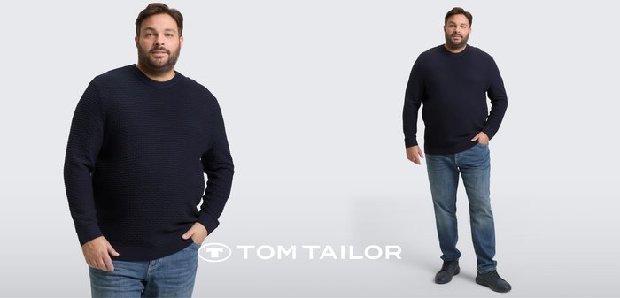 Mężczyzna w granatowym, teksturowanym swetrze, niebieskich dżinsach i czarnych butach, pozujący na tle jasnoszarego tła z logo Tom Tailor.