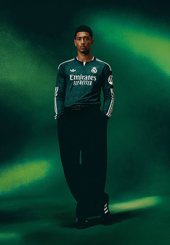 Mann, der ein dunkelgrünes Real Madrid Fußballtrikot trägt, steht mit den Händen in den Taschen vor einem grünen Farbverlauf-Hintergrund.